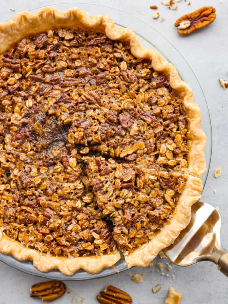 The top view of an oatmeal pecan pie. A slice is cut out and about to be served with a silver pie server. 