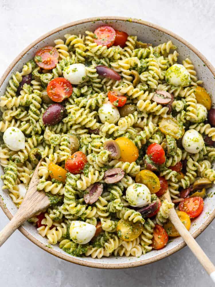 The top view of a bowl of pasta salad with 2 wooden spoons. 