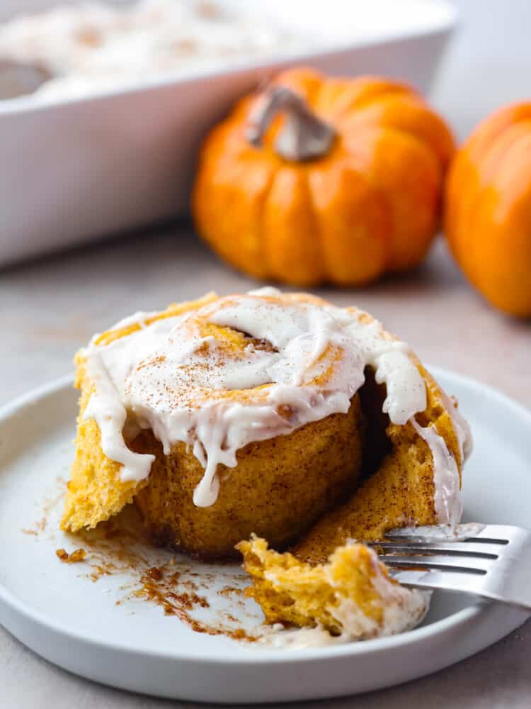 Closeup of a pumpkin cinnamon roll served on a white plate.