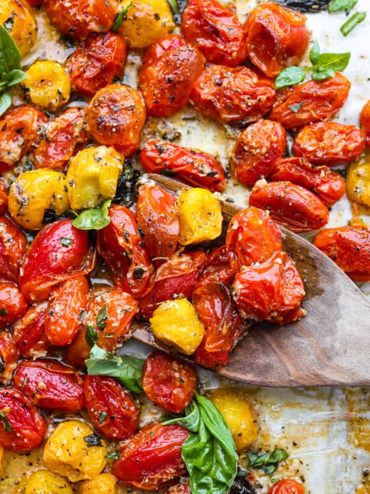 A close up of roasted cherry tomatoes being scooped up with a wooden spoon. 