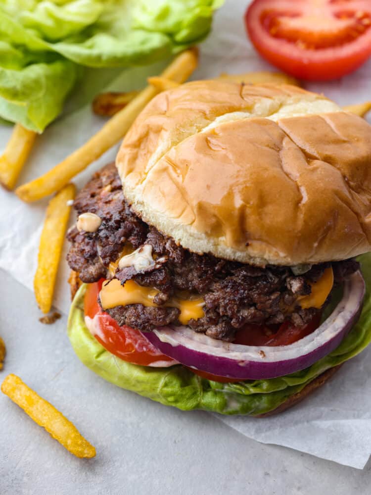 Top view of smash burger with top bun slightly off centered so you can see the meat, onion, lettuce, and cheese.  Fries on the side.