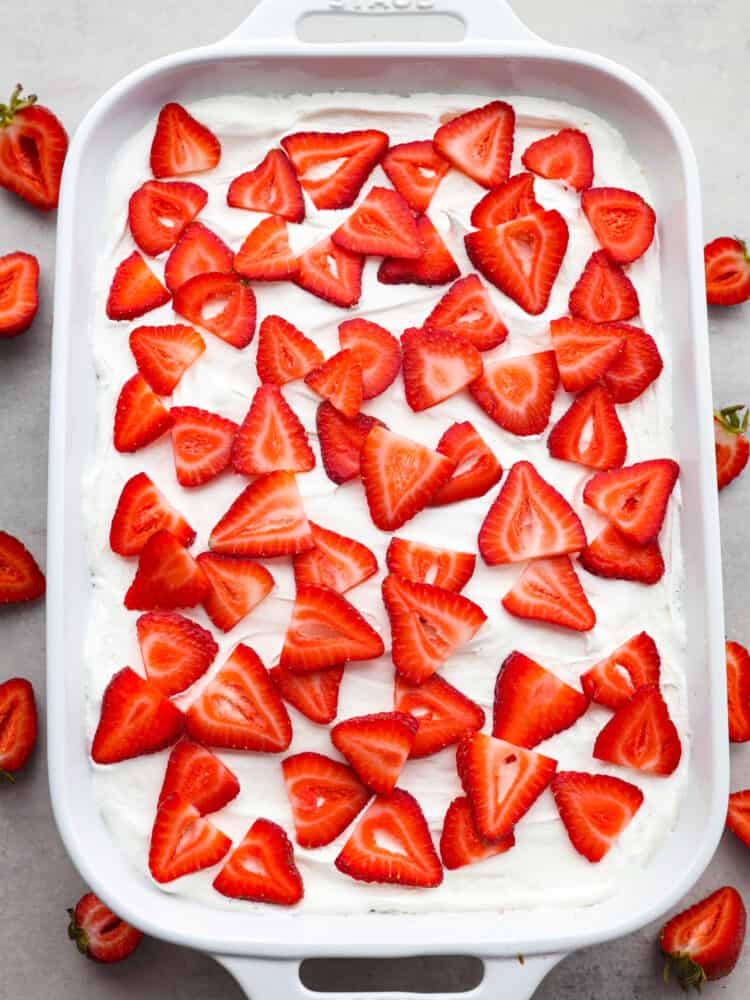 The top view of a strawberry poke cake in the cake pan, topped with cool whip and sliced strawberries. 