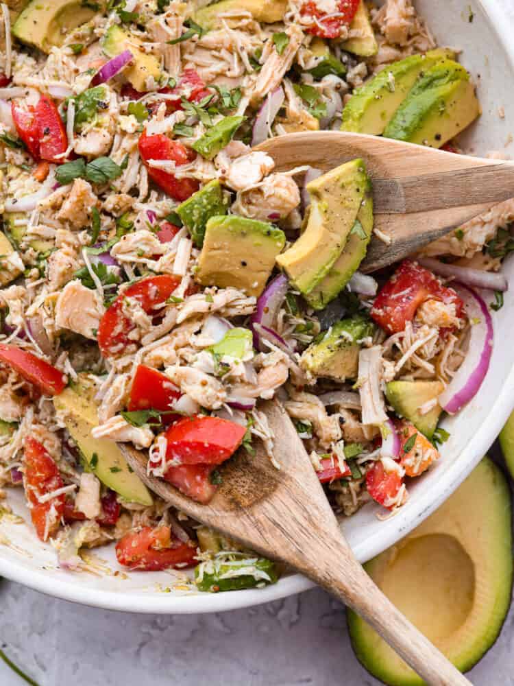 A bowl of tuna salad being mixed with two wooden spoons.