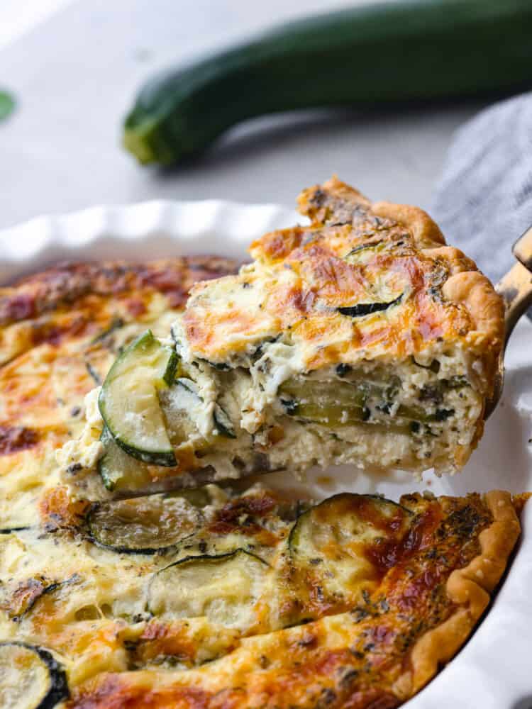 A slice of zucchini quiche being taken out of the serving dish with a pie server. 