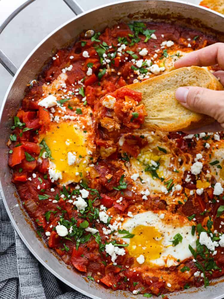 A piece of bread being dipped into the egg and tomato mixture.