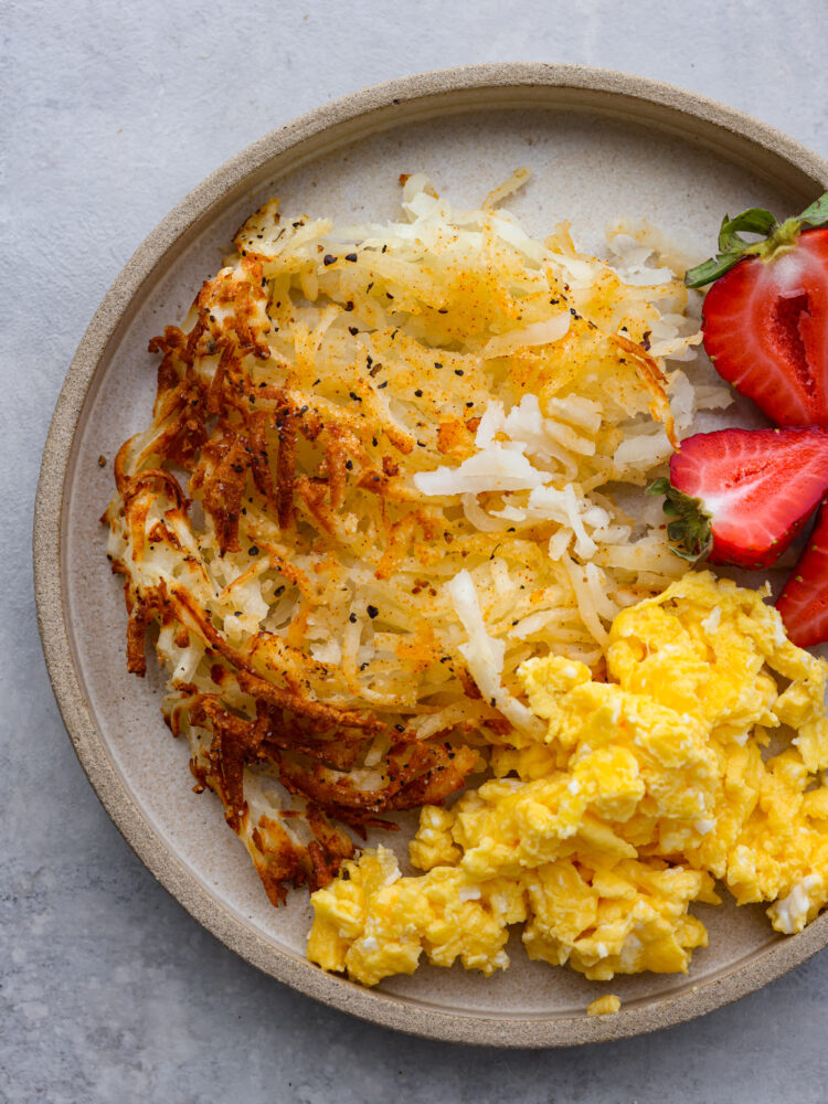 Top view photo of hash browns on a tan colored plate.  Sliced whole strawberries garnished on the side.