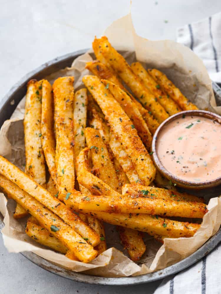 Closeup of jicama fries, served with dipping sauce in a gray bowl.