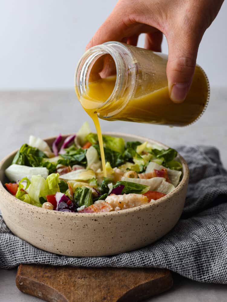 Apple cider vinaigrette being poured over a salad.