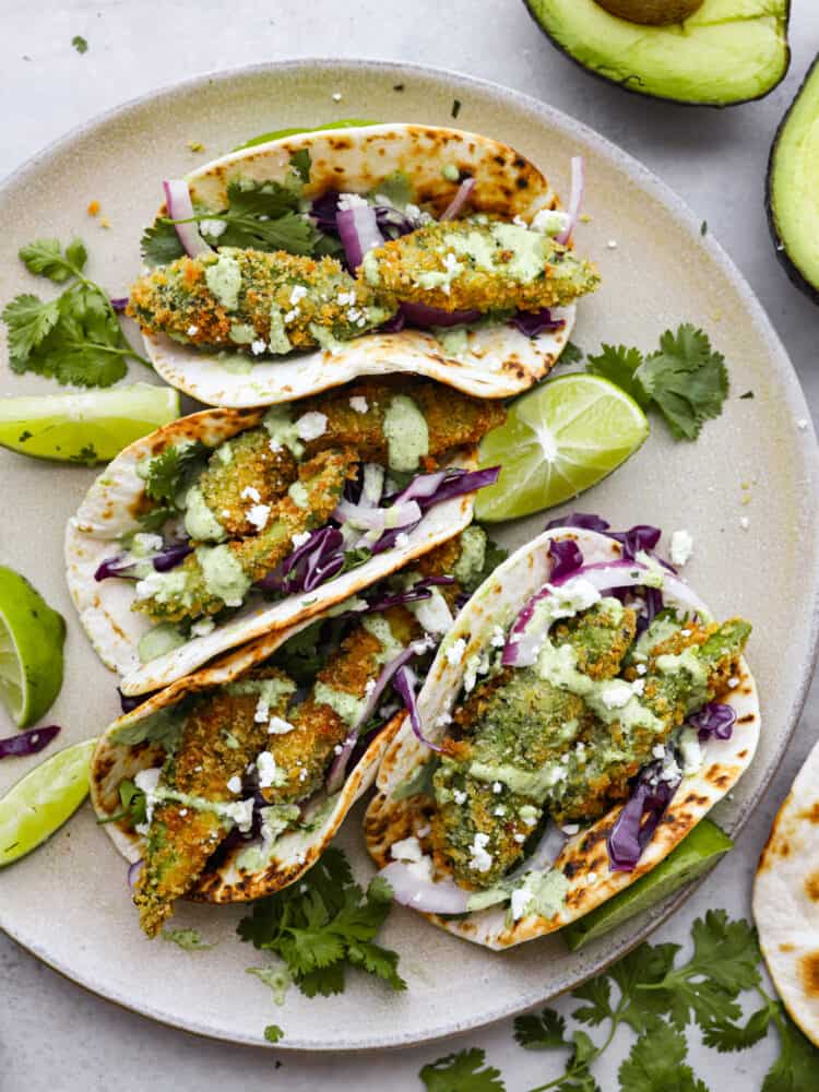 Top-down view of avocado tacos arranged on a white plate.