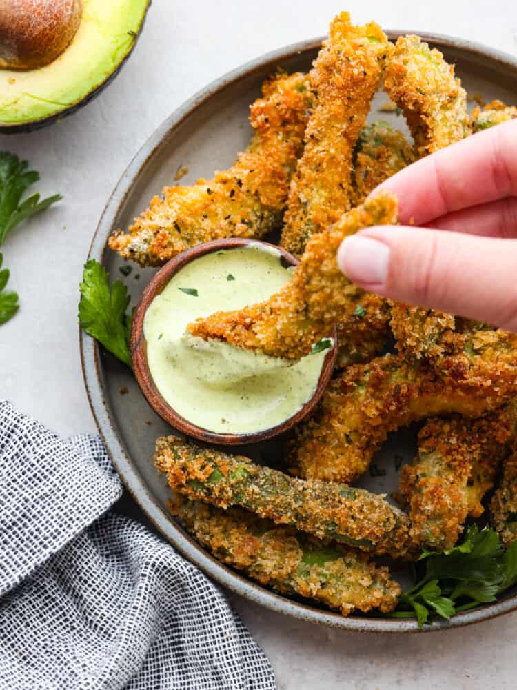 An avocado fry being dipped into some avocado ranch. 