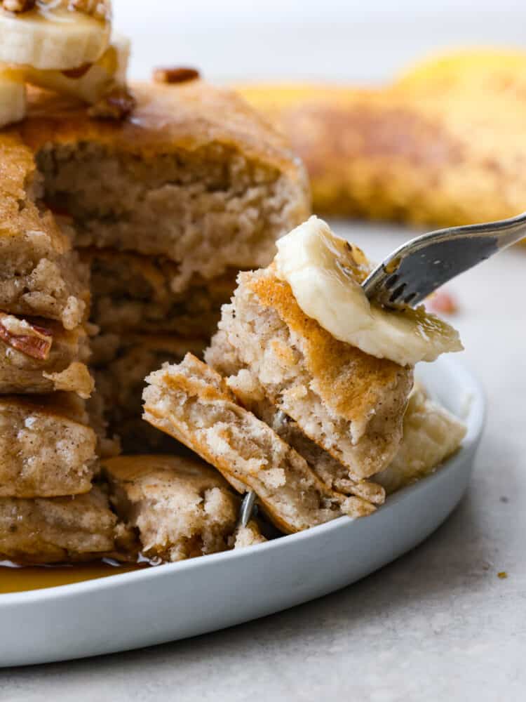 Banana pancakes on a plate with a fork cutting out a bite. 