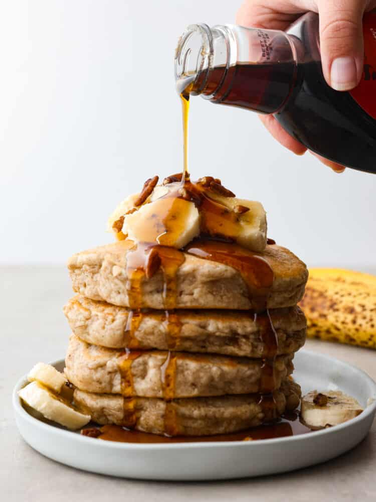 A stack of banana pancakes with a homemade vanilla maple glaze being poured on top. 