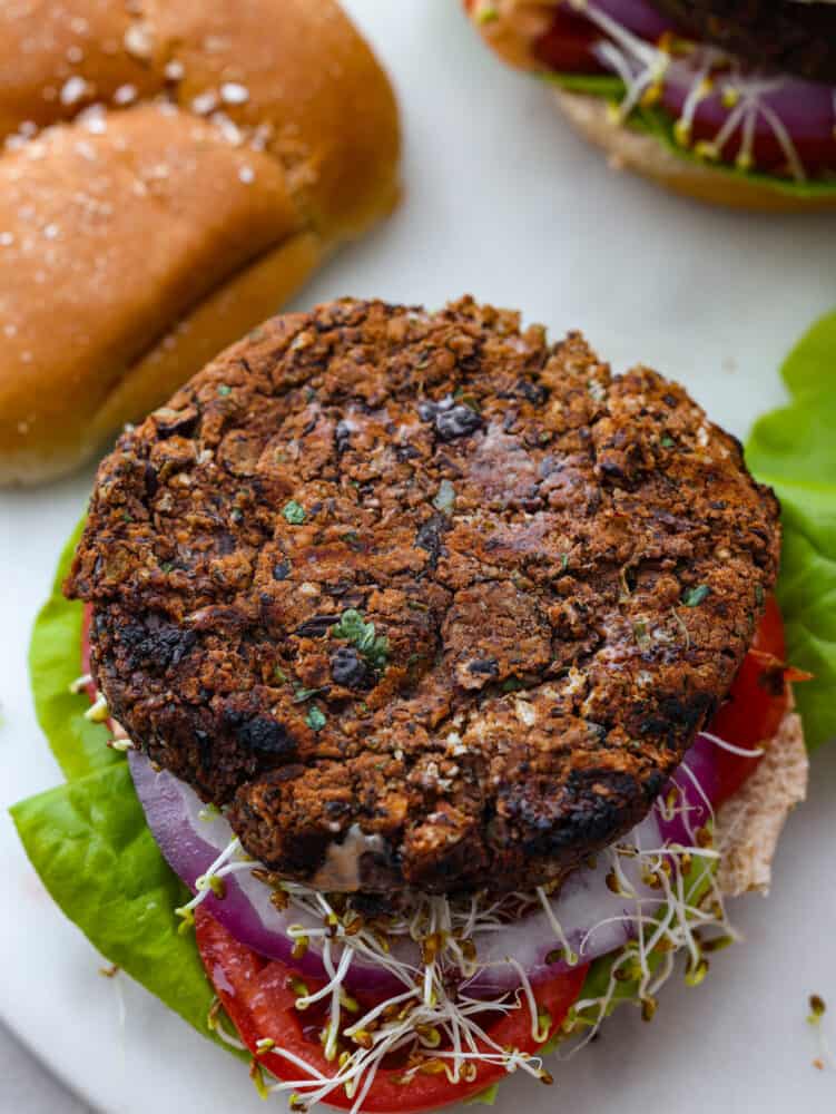 Top view of a black bean burger layered on top of a bun, lettuce, red onion, tomato slice, and sprouts.  The top of the bun is removed.