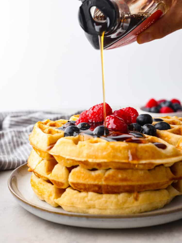 Syrup being poured on 3 waffles stacked on top of each other.