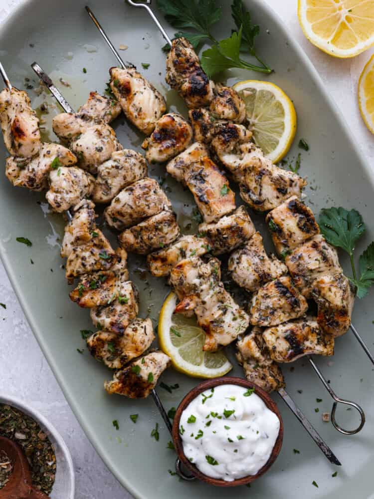 Top-down view of chicken souvlaki in a white dish, garnished with lemons.