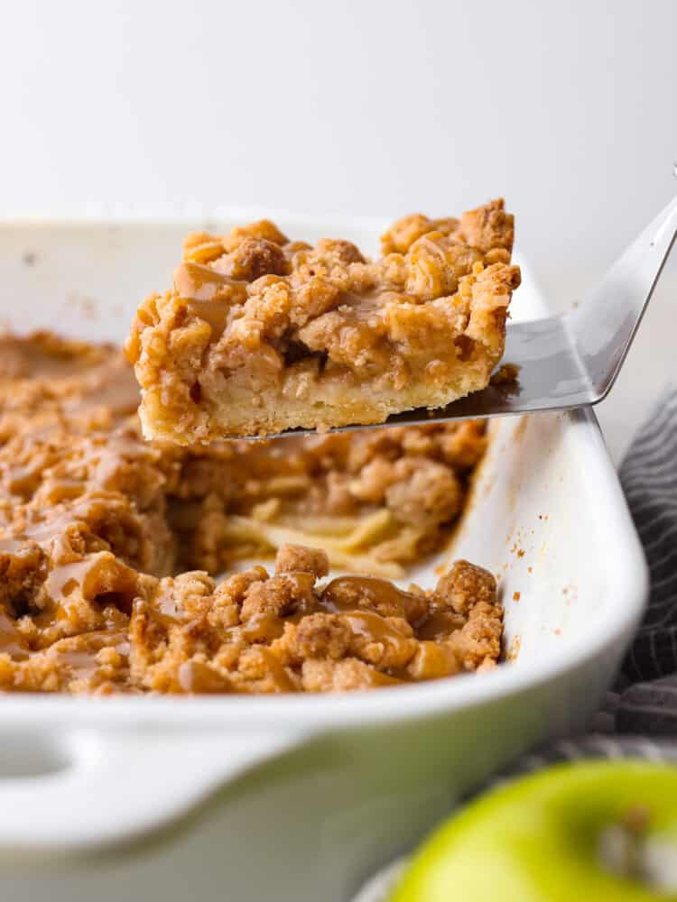 A caramel apple pie bar being taken out and served from the baking dish. 