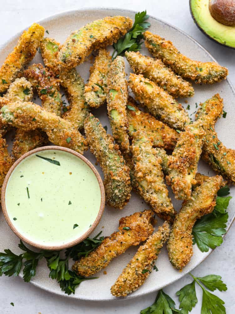 Top-down view of fried avocado slices on a gray plate served with dipping sauce.