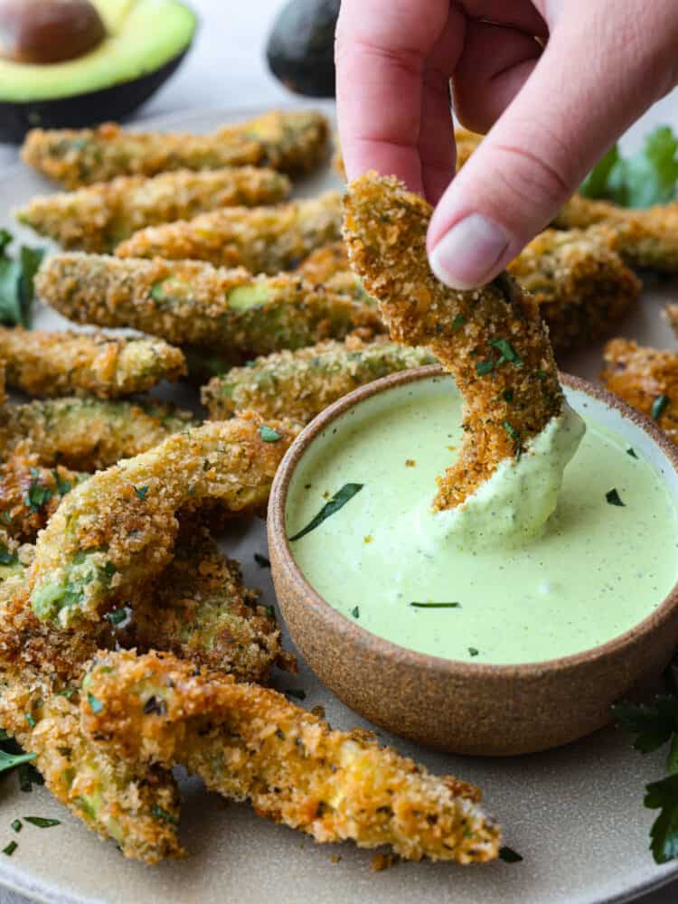 Closeup of an avocado fry being dipped in sauce.