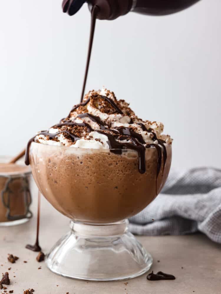 Chocolate syrup being poured over a cup of frozen hot chocolate.