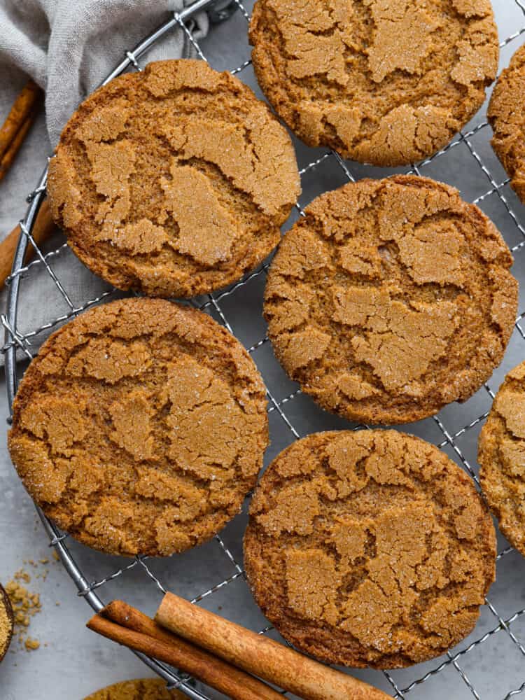 Gingersnap cookies on a wire rack with cinnamon sticks.