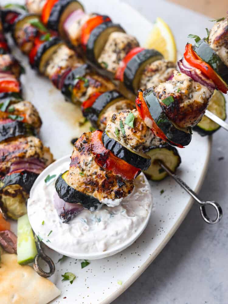 Close up photo of a Greek chicken kabob dipping in a bowl of tzatziki sauce.