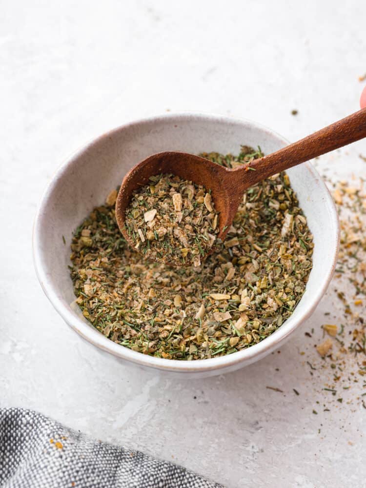 Scooping up Greek seasoning with a wooden spoon.