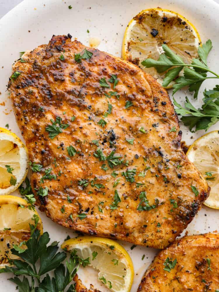 Close up view of grilled swordfish on a white platter.  The swordfish is garnished with parsley and grilled lemon slices.