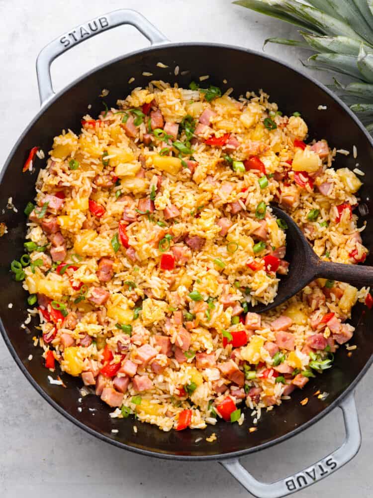 The top view of Hawaiian fried rice cooked in a skillet with a wooden spoon. 