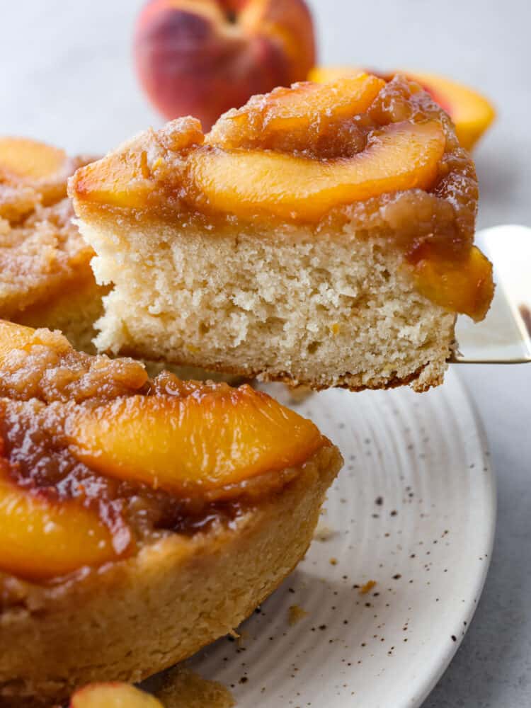 The side view of a slice of peach upside down cake being taken out with a cake server. 