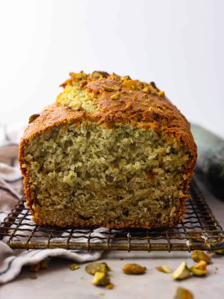 The side view of a loaf of piztachio zucchini bread on a cooling rack with the end cut off. 