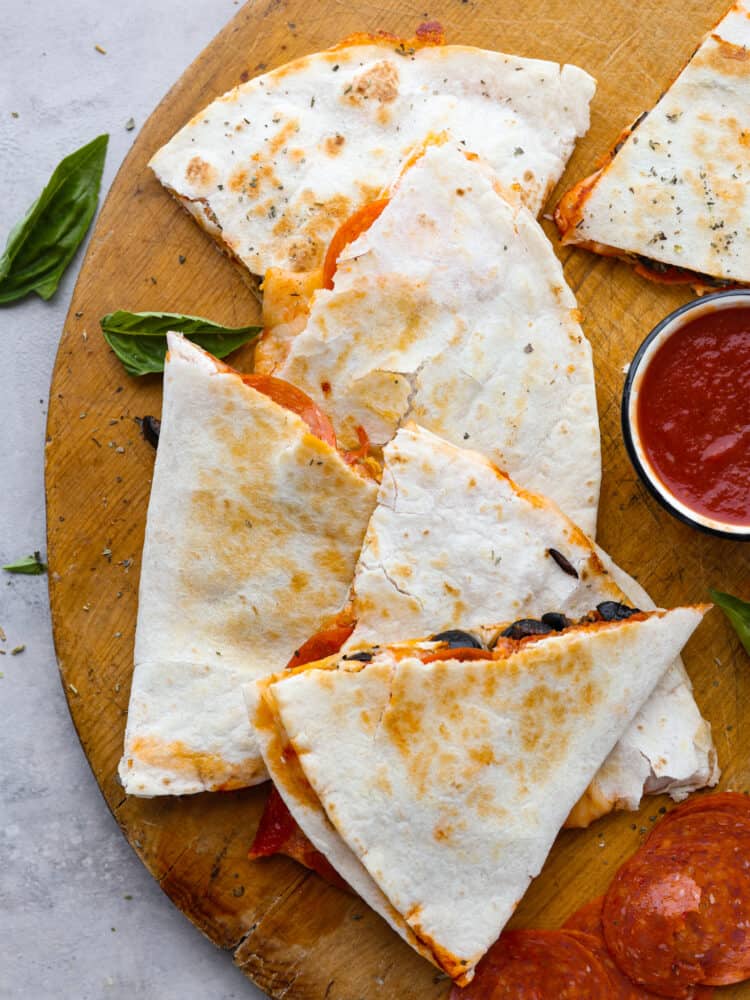 Slices of a pizza quesadilla on a wooden cutting board next to some marinara dipping sauce. 