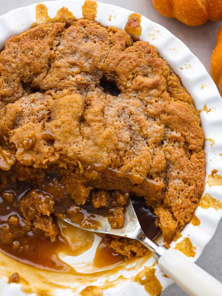 Top-down view of pumpkin pudding cake in a white serving dish. A scoop is taken out of it.