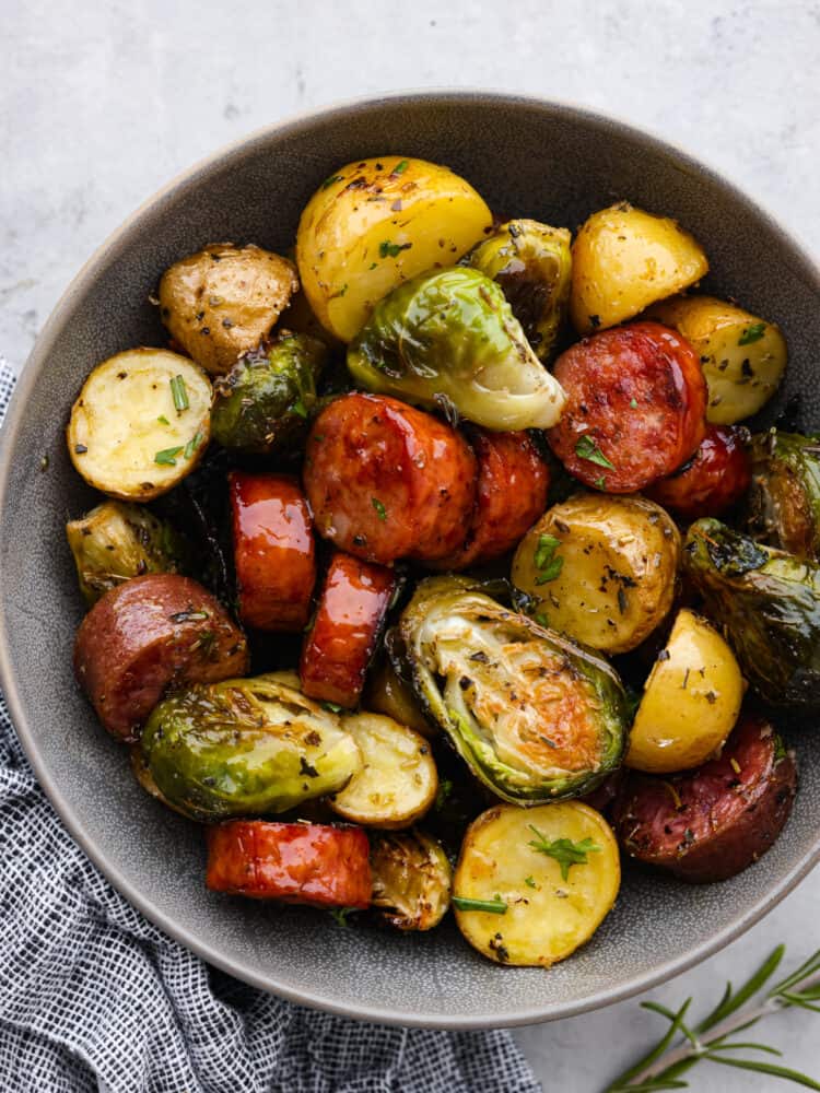 Sausage, Brussel sprouts and potatoes all cooked and seasoned and in a gray bowl. 