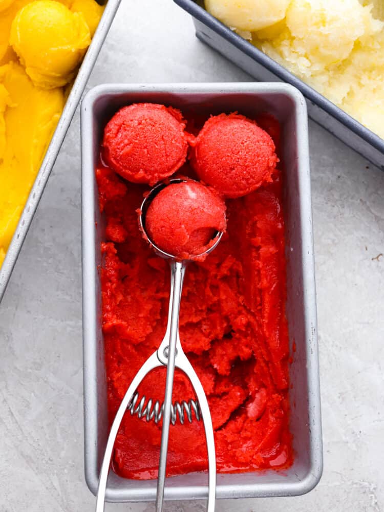 The top vew of strawberry sorbet in a bread pan with a scoop scooping out the sorbet. 