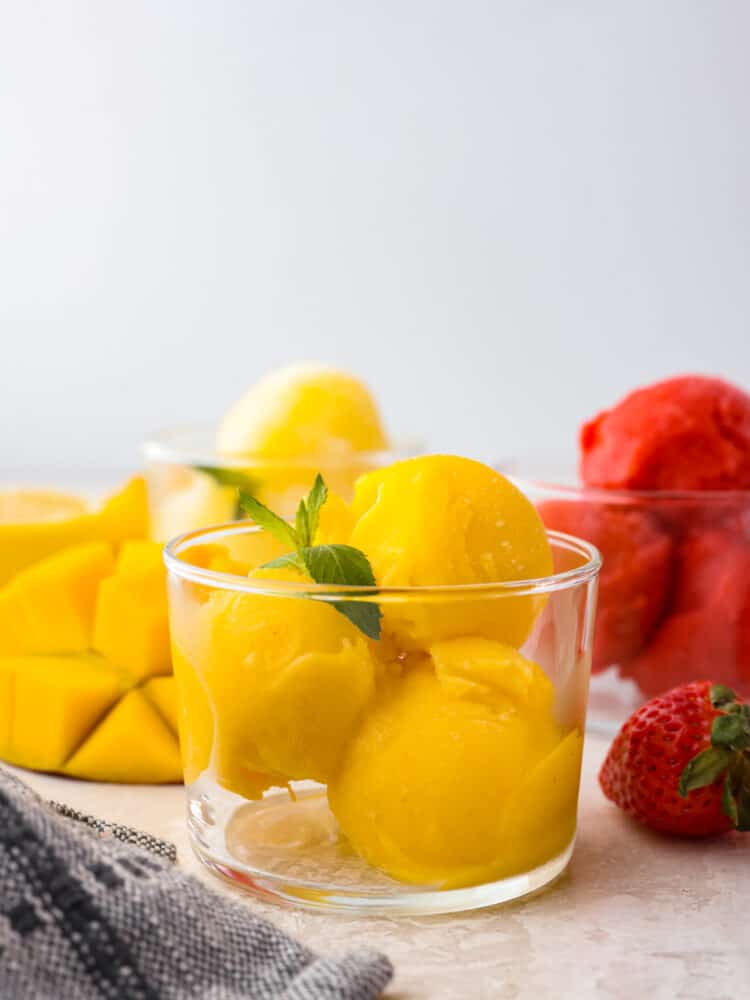 A glass cup with a few scoops of homemade mango sorbet with a mint leaf on top. 