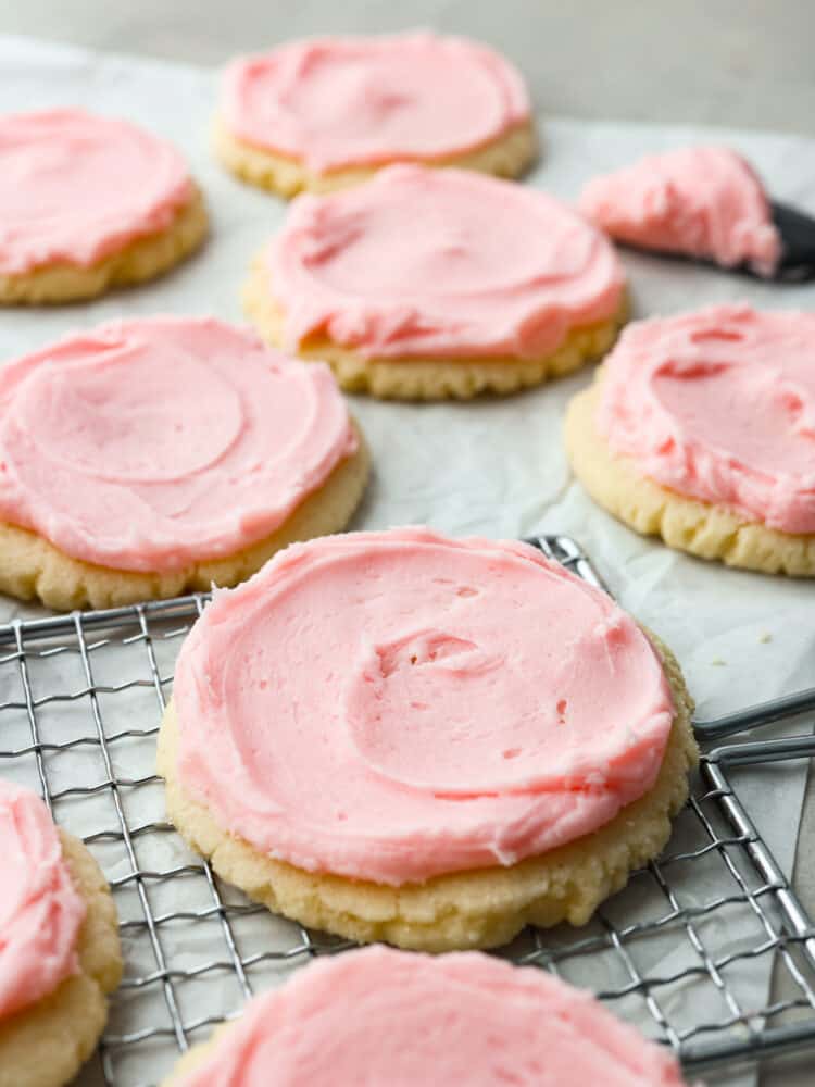 Sugar cookies with pink frosting on parchment paper and a cooling rack. 