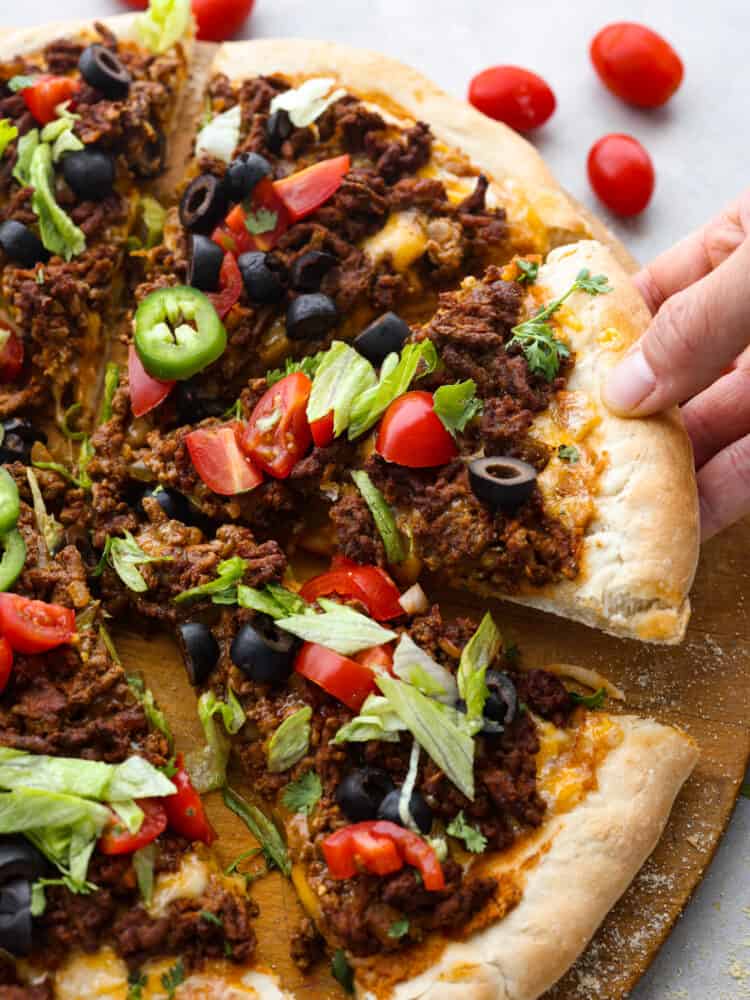 A slice of taco pizza being picked up off of the serving board.