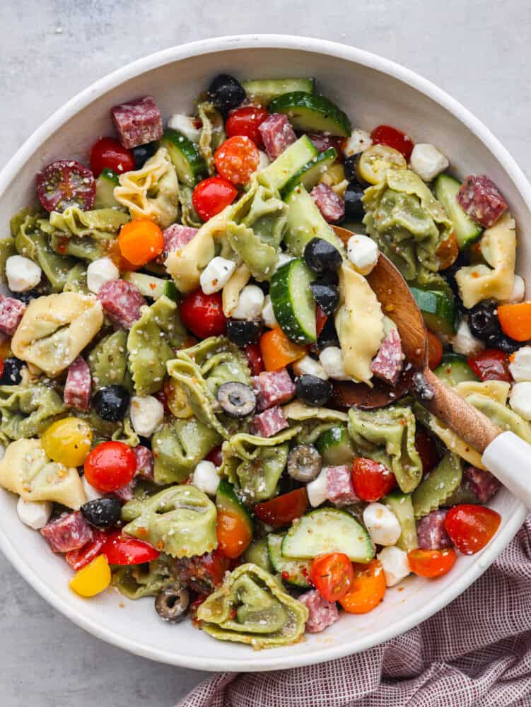 Top view of tortellini pasta salad in a bowl with a wooden spoon. 