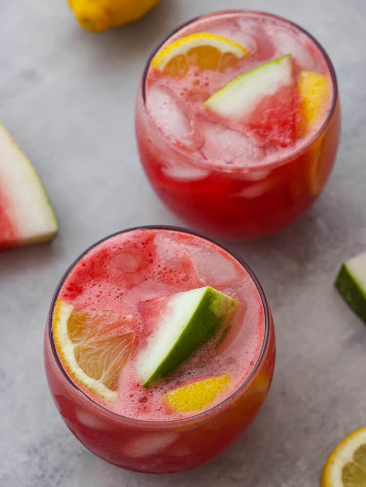 Top-down view of 2 cups of watermelon lemonade, garnished with lemon and watermelon slices.