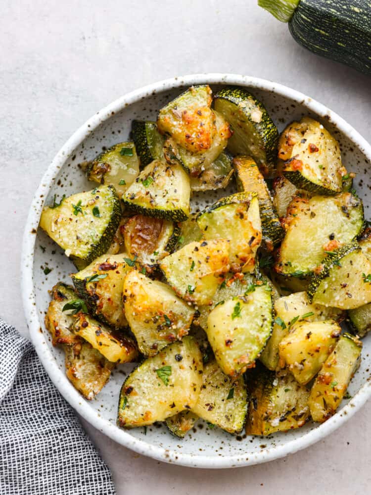 A whte speckled bowl filled with cooked zucchini slices. 