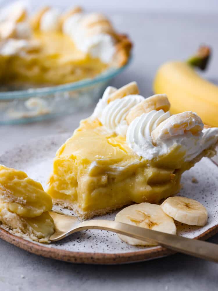 Closeup of a banana cream pie slice with a bite taken out of it.