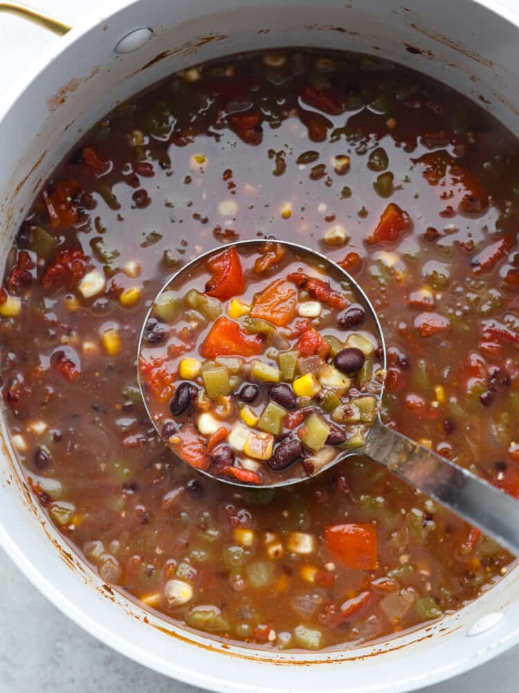 Black bean soup being served out of a large pot with a ladle.