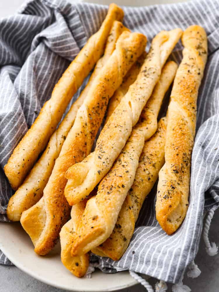 Cooked bread twists in a basket with a blue and white striped towel. 