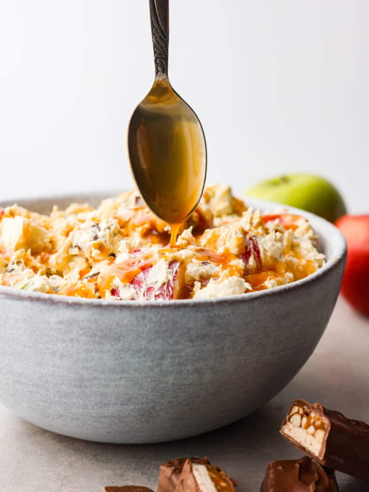 Snickers salad in a bowl with a spoon drizzling on some caramel sauce. 