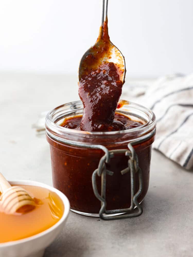 A jar of honey chipotle sauce with a spoon scooping some out. 