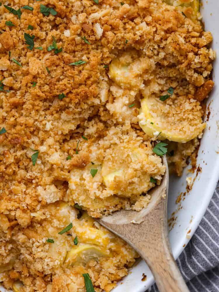 A close up of squash casserole with a wooden spoon. 