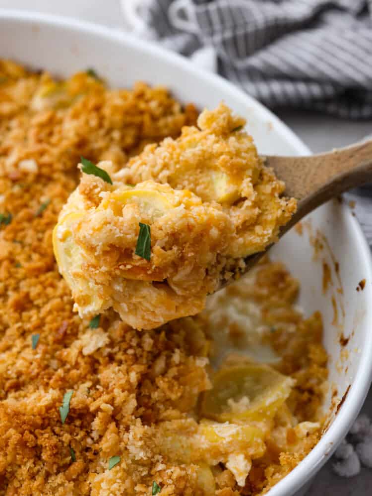 Squash casserole being scopped out with a wooden spoon. 