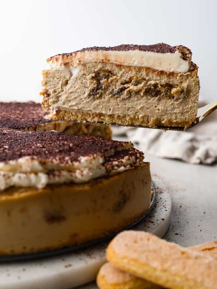 The side view of a cheesecake with a slice being taken out. 