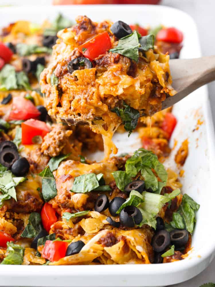 Taco casserole being scooped out with a wooden spoon. 