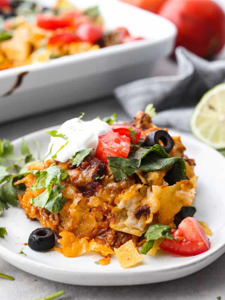 Some taco casserole on a plate loaded with veggies and sour cream. 